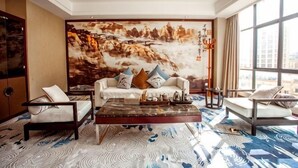 A spacious living room with a large painting, a sofa set, a coffee table, and a view through large windows. - Yongqian Hotel (Yongde)