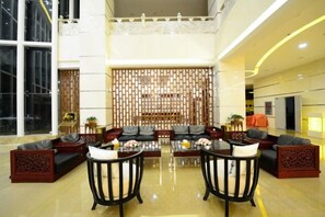 A spacious lobby with a high ceiling, a central seating area with sofas and tables, and a decorative wall in the background.