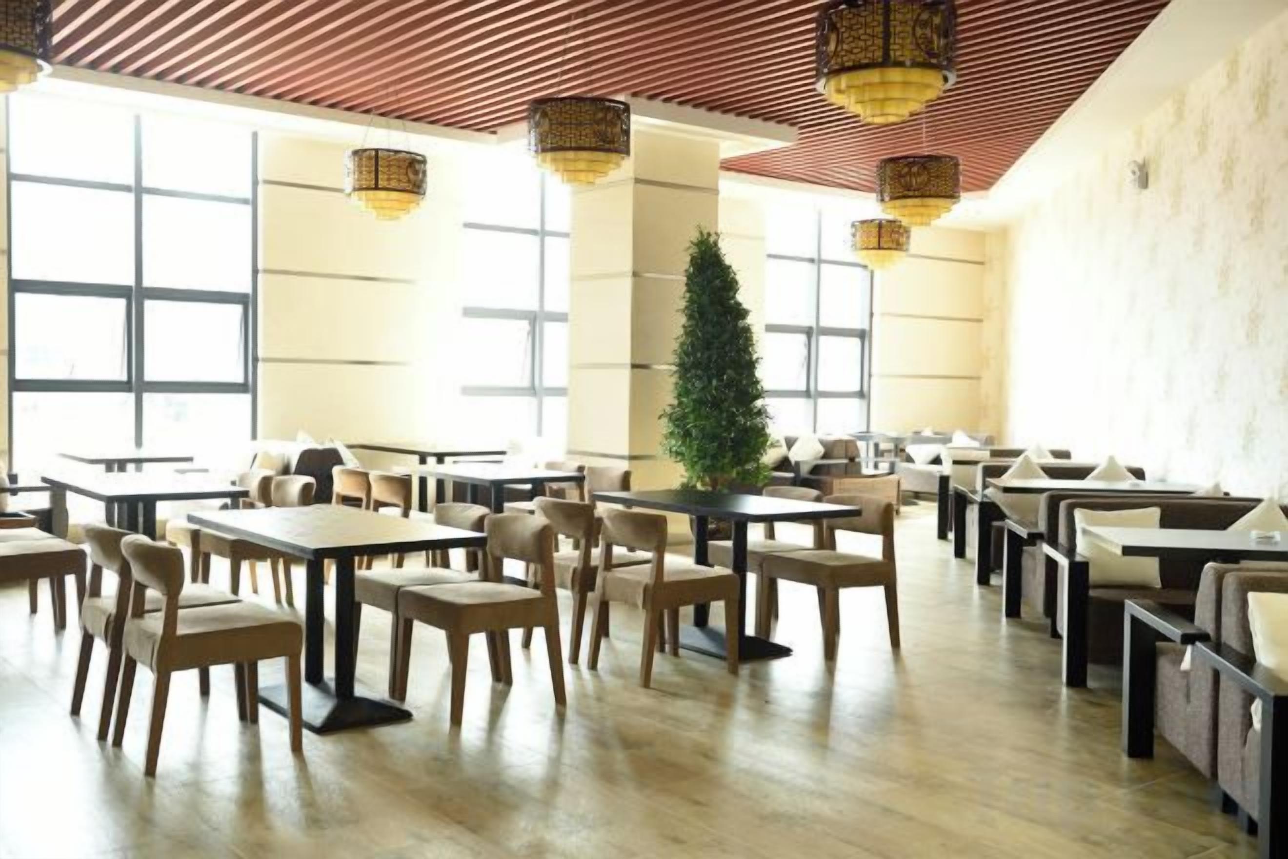 A spacious dining area with multiple tables and chairs, large windows, and a central decorative tree.