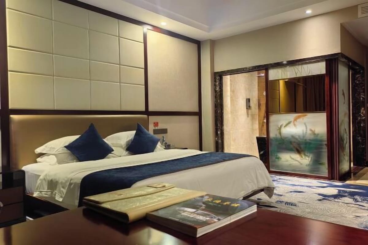 A hotel room with a large bed, a wooden nightstand, and a painting on the wall.