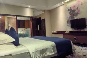 A hotel room with a bed, a television, a wall-mounted TV, and a door leading to another room.