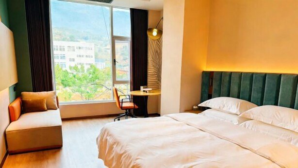 A hotel room with a bed, a desk, and a view of buildings through the window. - Yongqian Hotel (Yongde)