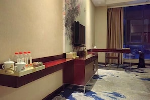 A hotel room with a reception desk, a television, a window with curtains, and a patterned carpet.