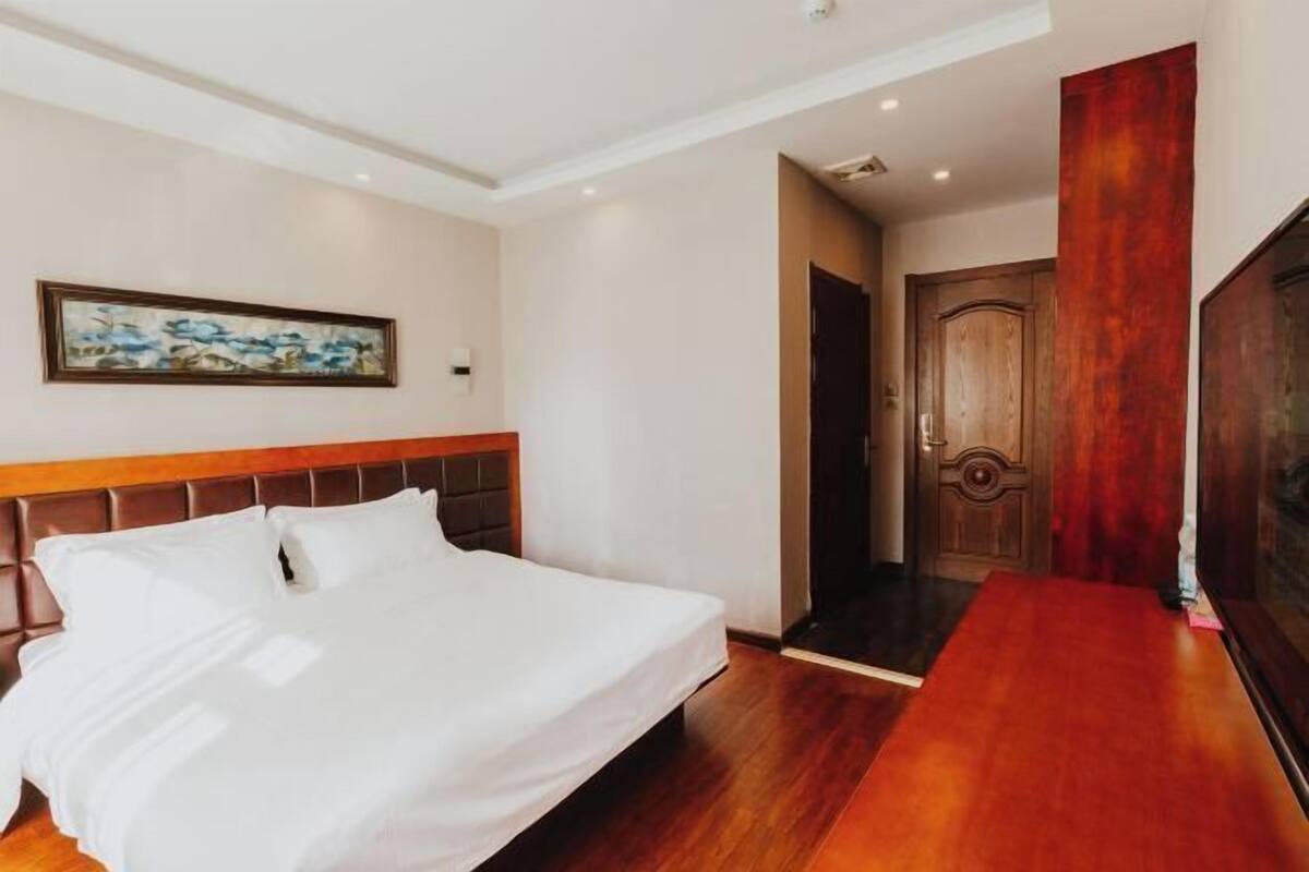 Ein Hotelzimmer mit einem großen Bett, einem Holzkopfende, einem Bild an der Wand und einer Holztür.