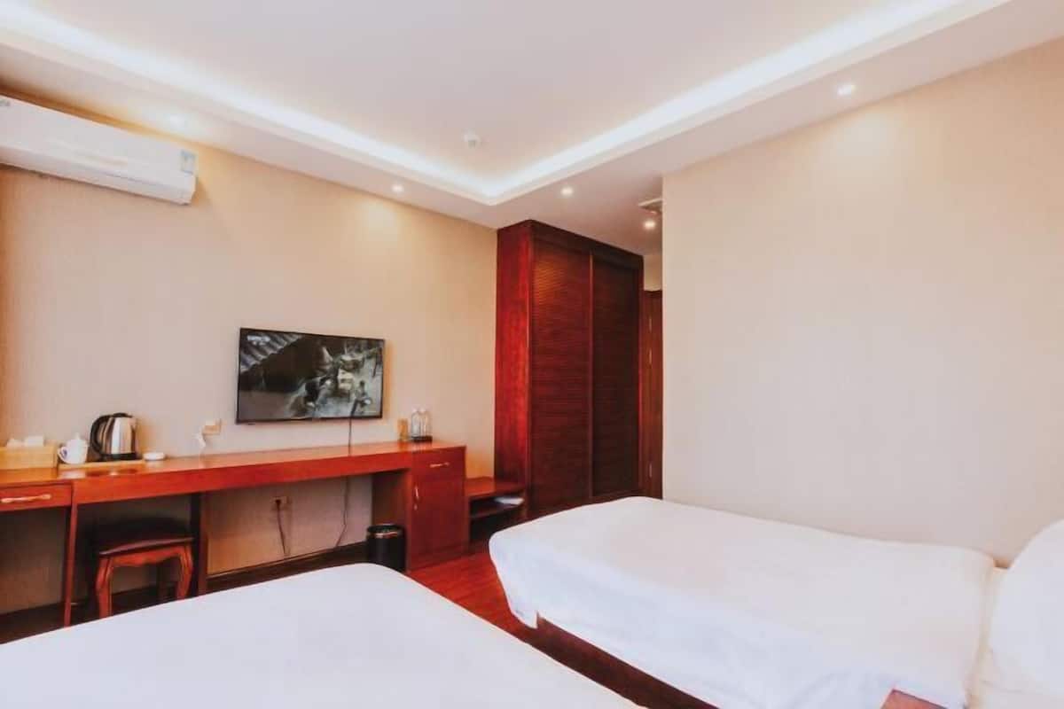 Ein Hotelzimmer mit zwei Betten, einem Schreibtisch, einem Sessel, einem Fernseher und einem Kleiderschrank.