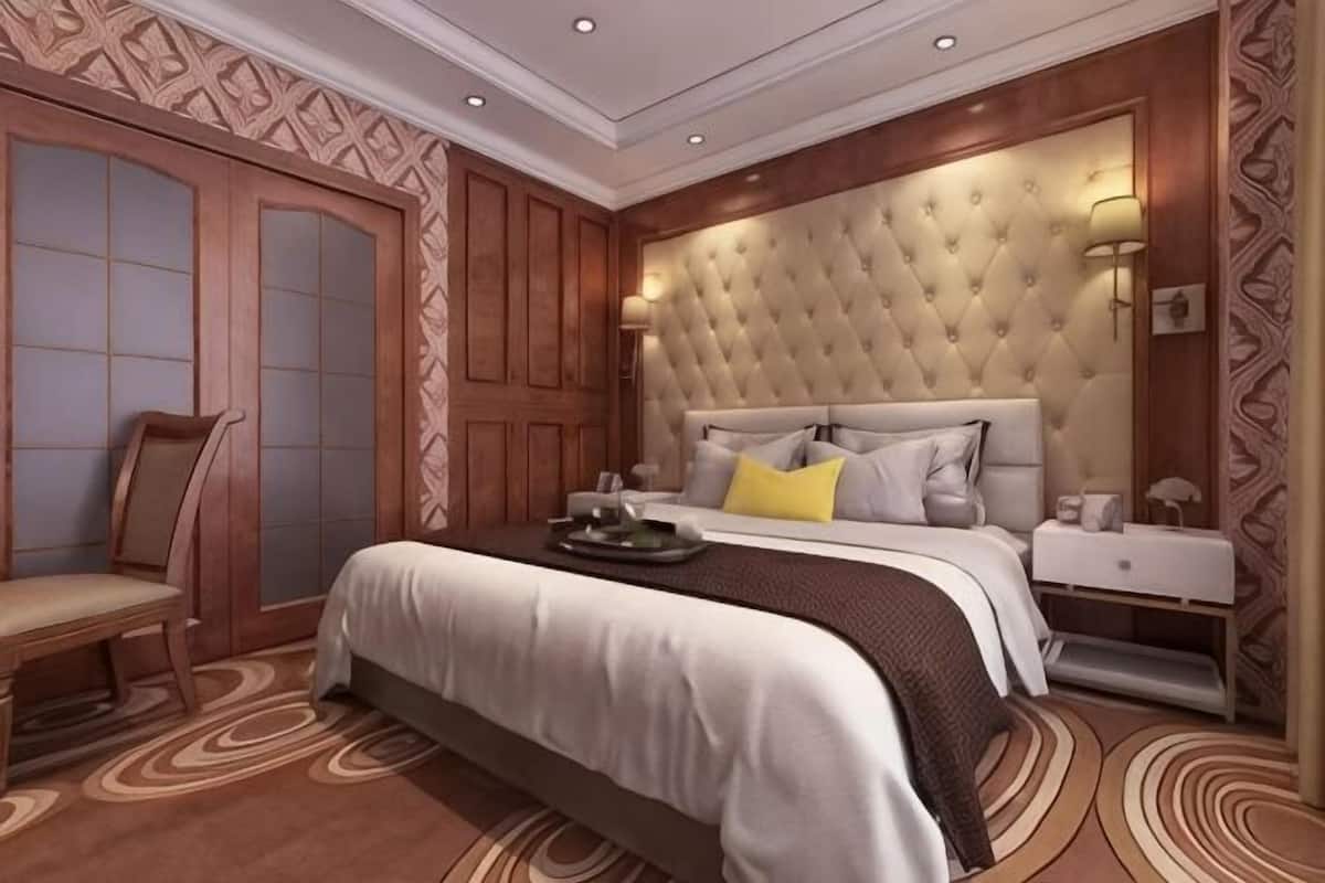 Ein Schlafzimmer mit einer gesteppten Kopfstütze, einem Holzstuhl, einem Nachttisch und einem gemusterten Teppich.