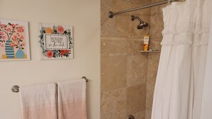 A bathroom with a shower, a towel rack with two towels, and two wall-mounted artworks.