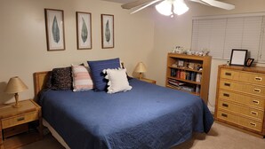 A bedroom with a bed, a nightstand, a dresser, a bookshelf, and a ceiling fan.