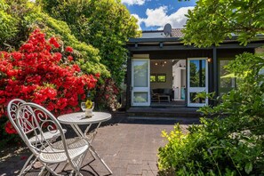A modern house with a glass door leading to a living area, surrounded by lush greenery and a patio with a table and chairs. - Elegant Town House with Wi-Fi, central location, easy walk to town (Taupō)