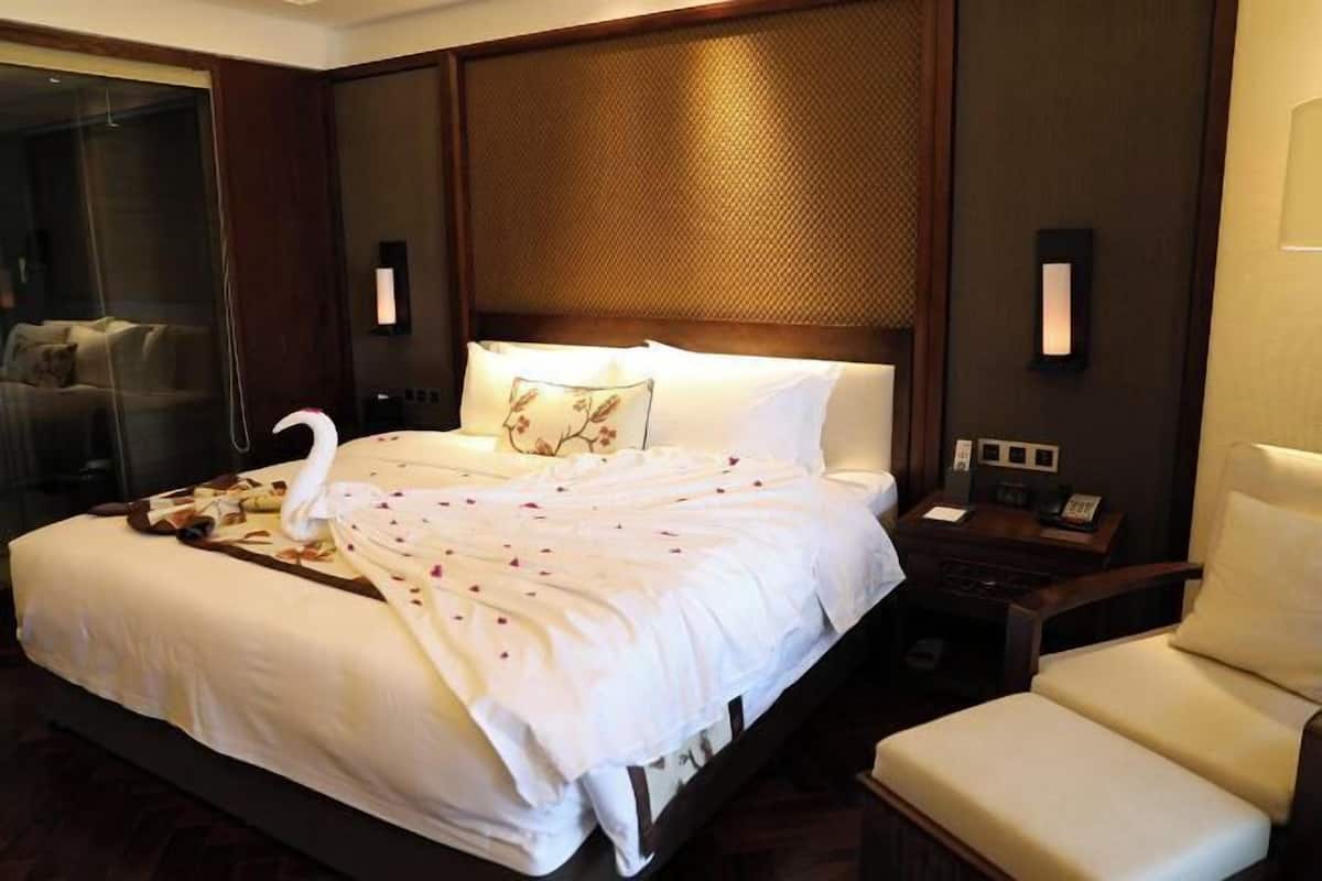 Habitación de hotel con una cama grande, una silla, una mesita de noche y un box de ducha de vidrio.