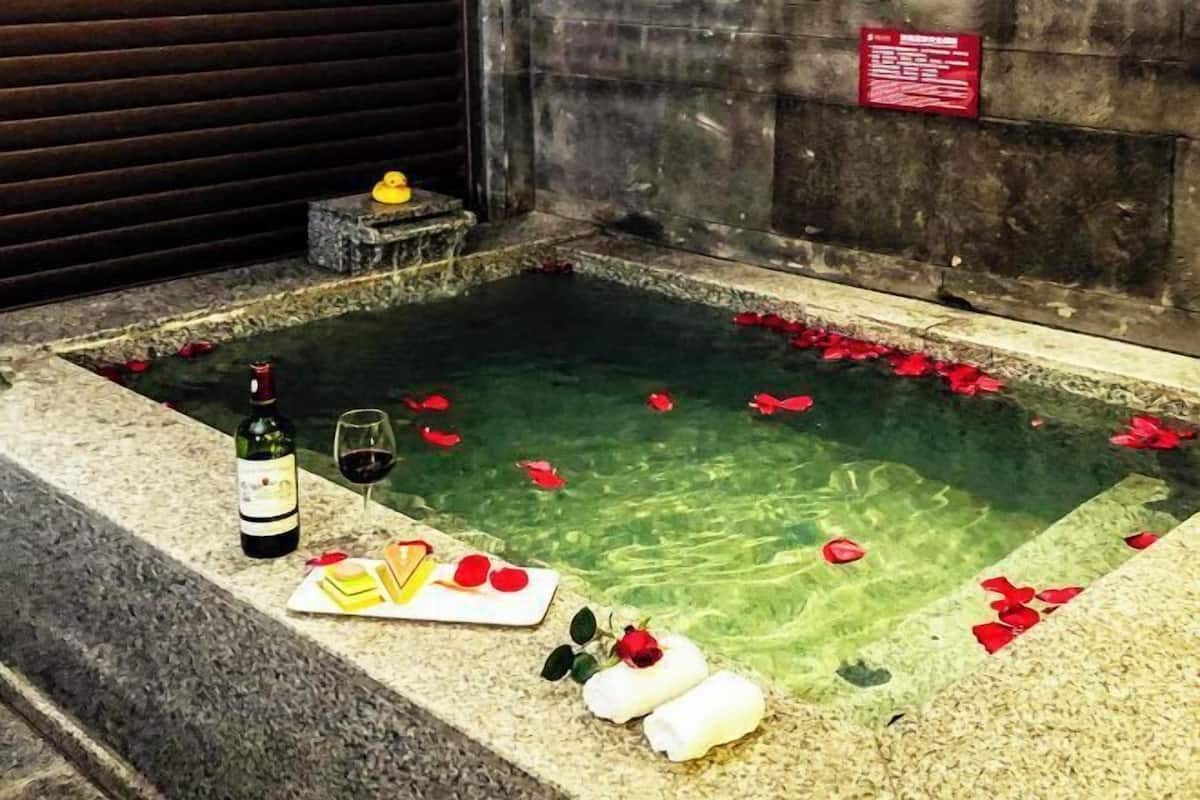 Zona de spa con hidromasaje, pétalos de rosa, una botella de vino y una copa.