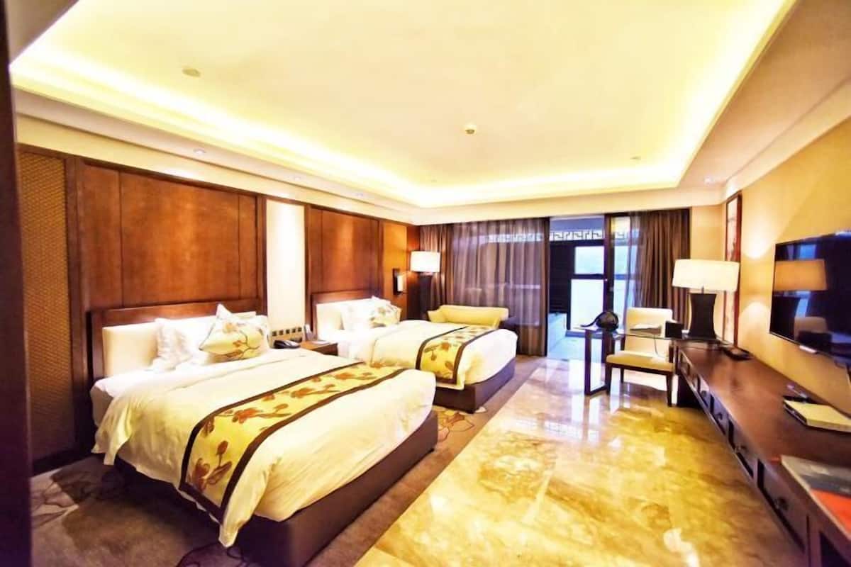 Habitación de hotel con dos camas, un televisor, un escritorio y un ventanal grande.