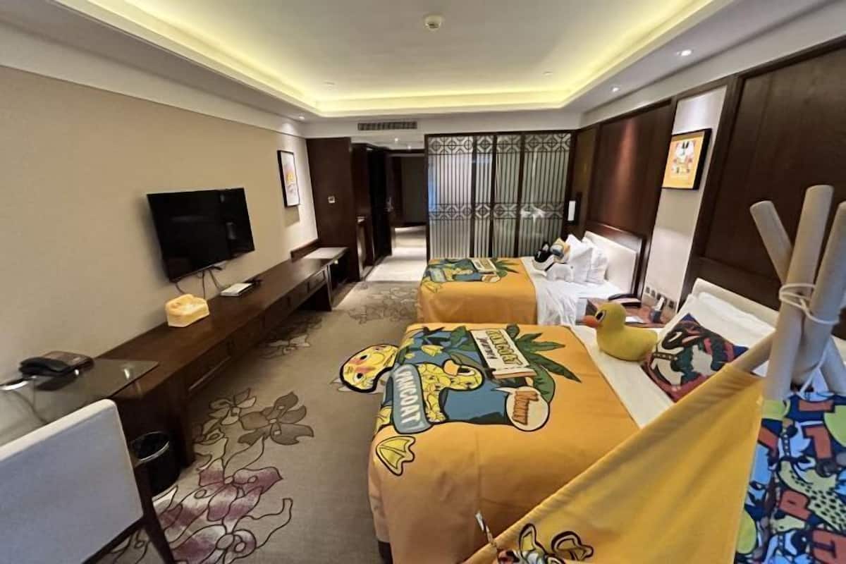 Habitación de hotel con dos camas, un escritorio, un televisor y un ventanal grande.