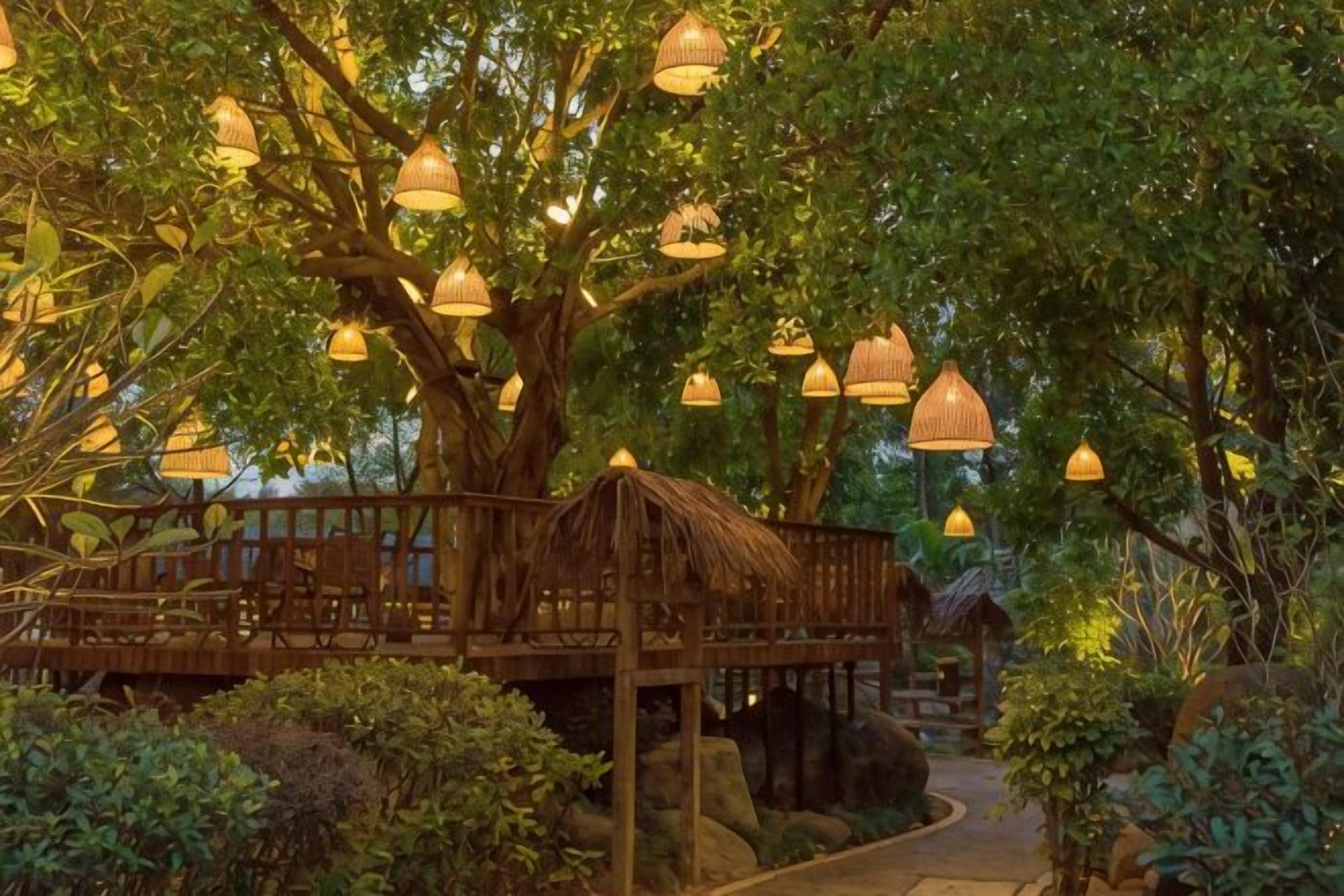 Een houten terras met hanglampen, omgeven door weelderige begroeiing en een rieten dakgebouw.