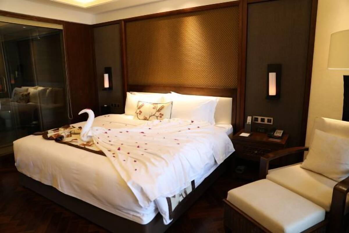 Habitación de hotel con una cama grande, una mesita de noche con lámpara, una silla y un separador de vidrio.