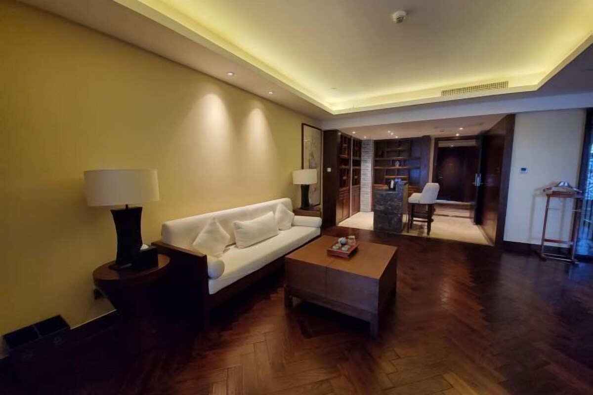 Ein modernes Wohnzimmer mit Sofa, Couchtisch und Lampen. Ein Holzboden und ein Küchenbereich sind im Hintergrund zu sehen.