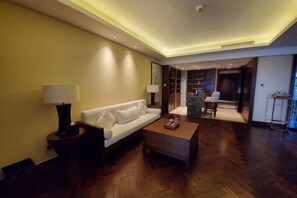 Ein modernes Wohnzimmer mit Sofa, Couchtisch und Lampen. Ein Holzboden und ein Küchenbereich sind im Hintergrund zu sehen.