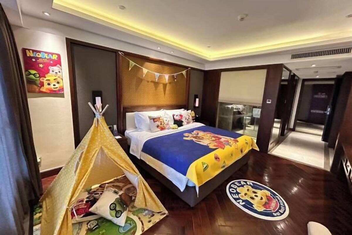 Una habitación de hotel con una cama, una tienda de campaña y un cartel con un oso de dibujos animados.