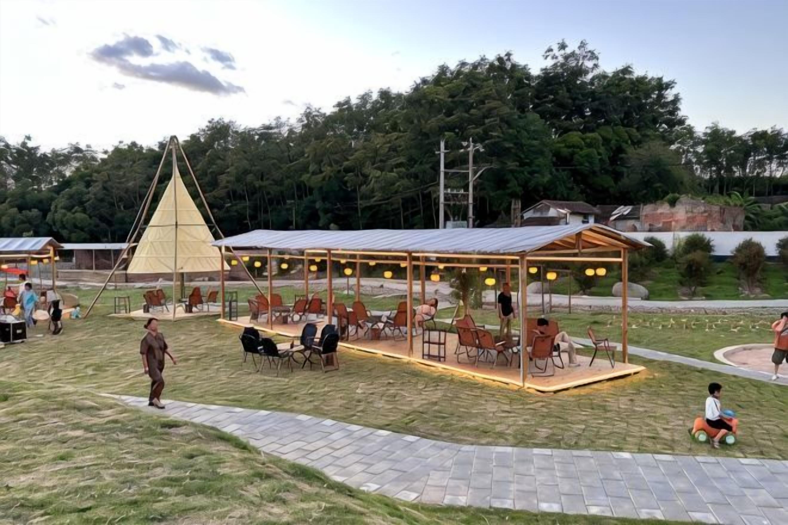 An outdoor seating area with tables and chairs, a covered pavilion, and a grassy field.