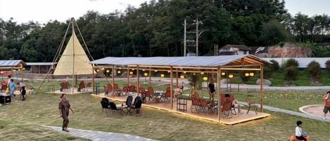 An outdoor seating area with tables and chairs, a covered pavilion, and a grassy field.