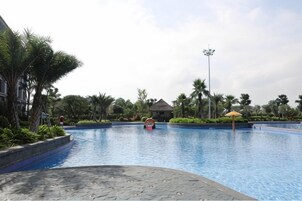 Una piscina con borde de baldosas, rodeada de vegetación tropical y una estructura con techo de paja.