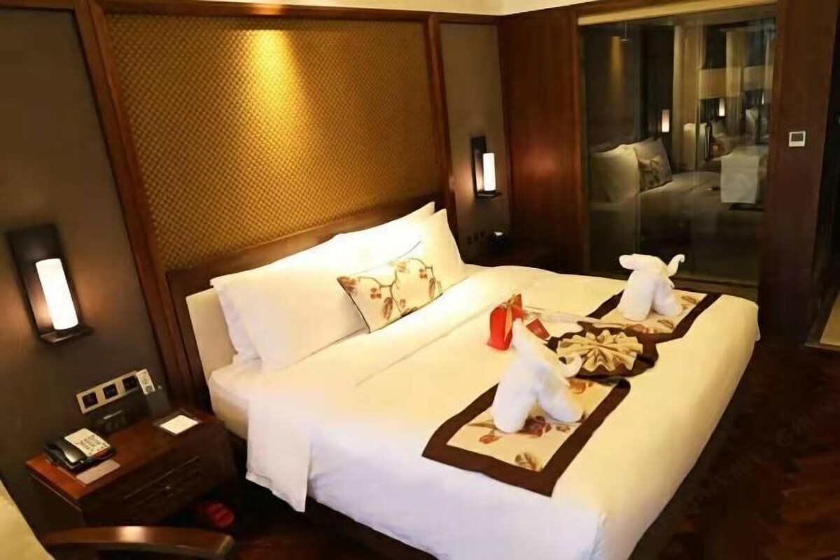 Ein Hotelzimmer mit einem großen Bett, einem Nachttisch mit Telefon und Blick auf eine Sitzecke durch eine Glastür.