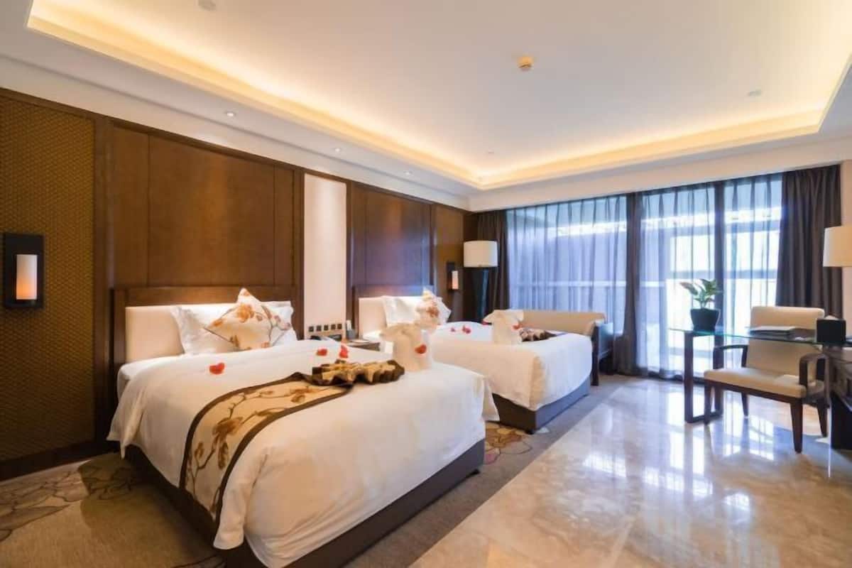 Habitación de hotel con dos camas, un área de descanso y un amplio ventanal con cortinas.