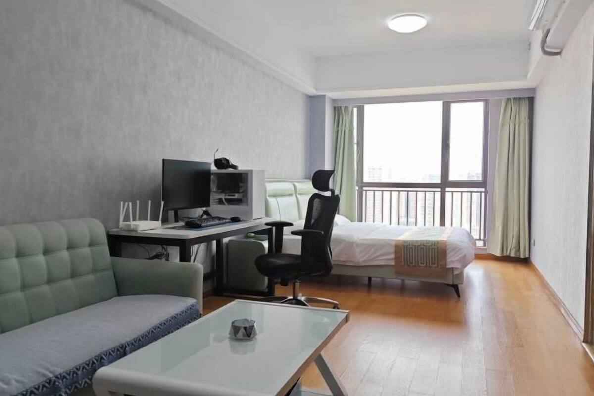Ein Hotelzimmer mit Bett, Schreibtisch mit Computer, Stuhl, Sofa und einem Fenster mit Vorhängen.