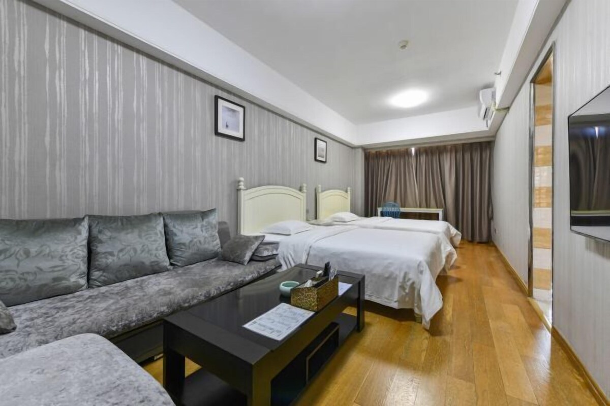 Ein Hotelzimmer mit Sofa, Bett, Nachttisch, Fernseher und einem Fenster mit Vorhängen.