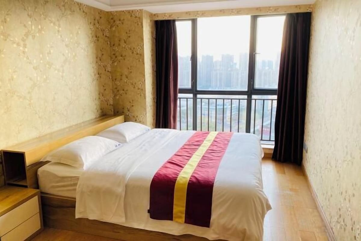 Ein Hotelzimmer mit einem großen Bett, einem Nachttisch, einem Fenster mit Blick auf Gebäude und einem Balkon.