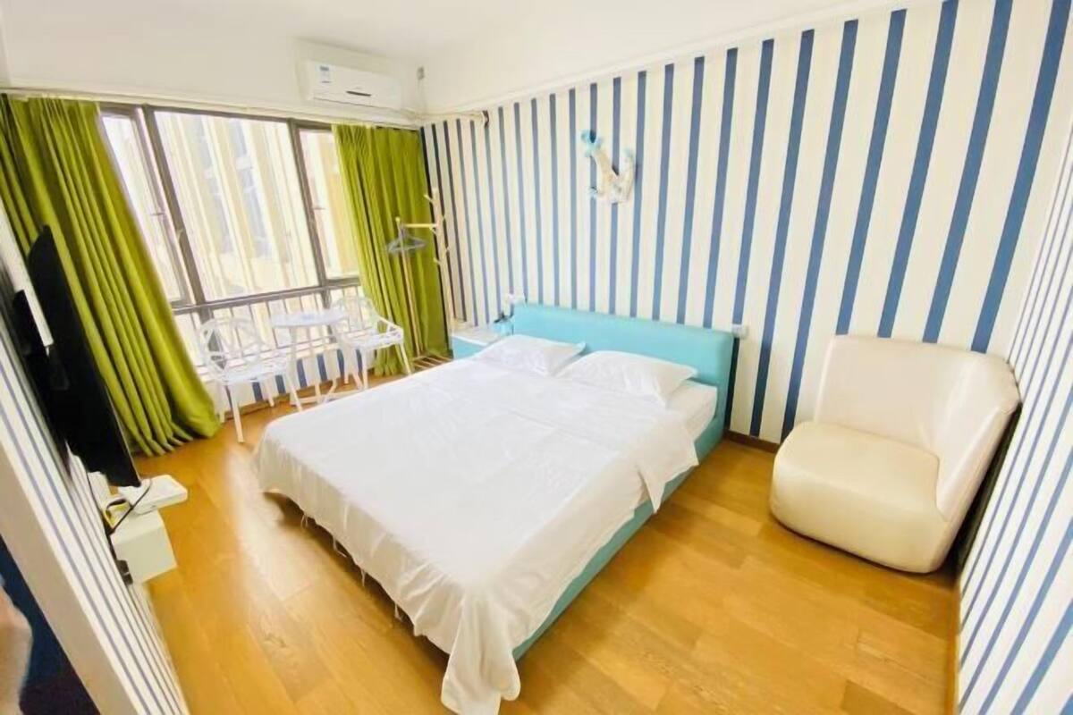 Ein Hotelzimmer mit Bett, Stuhl, Fenster mit Vorhängen und einer gestreiften Wand.