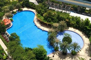 Une grande piscine de forme ovale, entourée d’une végétation luxuriante et de palmiers.