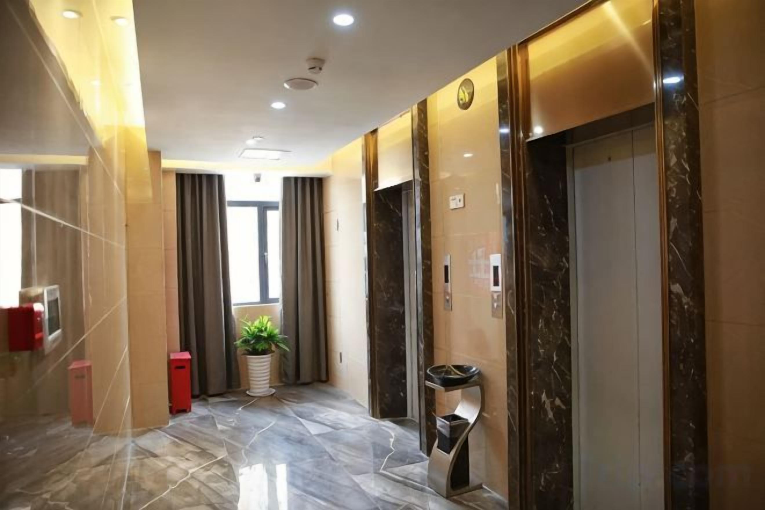A hotel lobby with a marble floor, a potted plant, an elevator, and a trash bin.