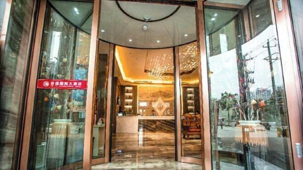 Entrada de un hotel con puertas de vidrio, mostrador de recepción y un candelabro.