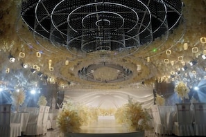 An indoor venue with a circular stage, decorative lighting, and floral arrangements. - Hefu International Hotel (Nanzhang)