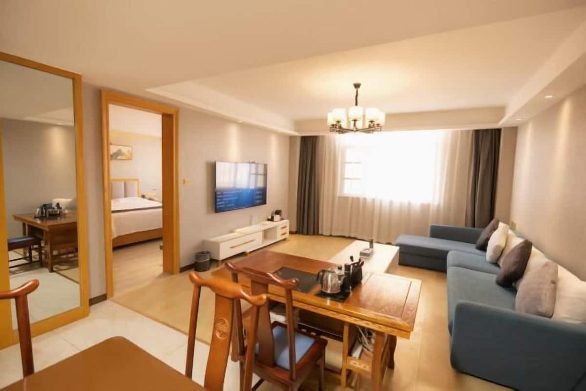 Ein Hotelzimmer mit Essbereich, einer Couch, einem Fernseher und einem großen Fenster mit Vorhängen.