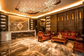 A lobby with a reception desk, seating area, and decorative wall panels. - Hefu International Hotel (Nanzhang)