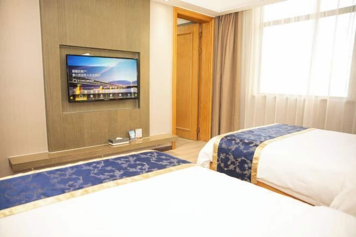 Ein Hotelzimmer mit zwei Betten, einem an der Wand befestigten Fernseher und einem Fenster mit Vorhängen.