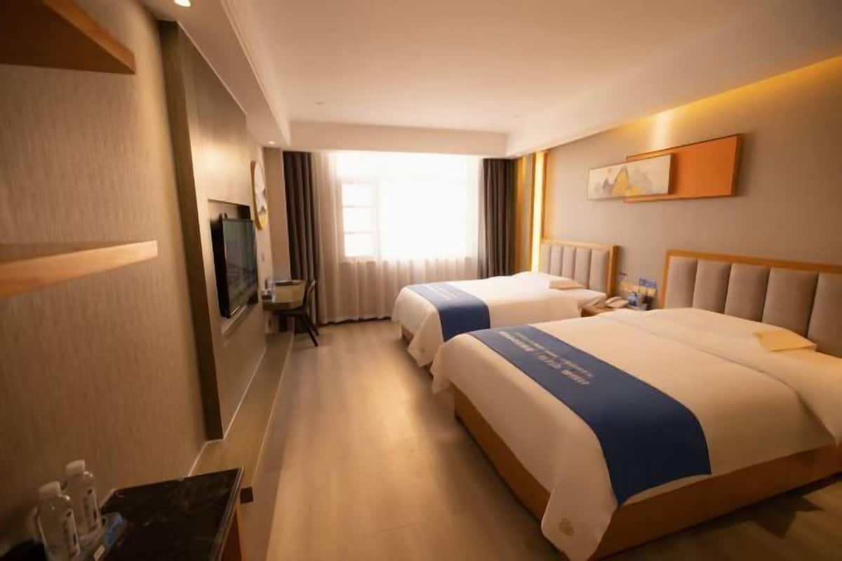 Ein Hotelzimmer mit zwei Betten, einem Schreibtisch, einem Fernseher und einem Fenster mit Vorhängen.