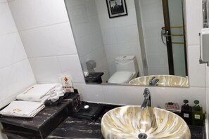 Une salle de bain avec un lavabo en marbre, des toilettes, un miroir et des serviettes rangées sur une étagère.