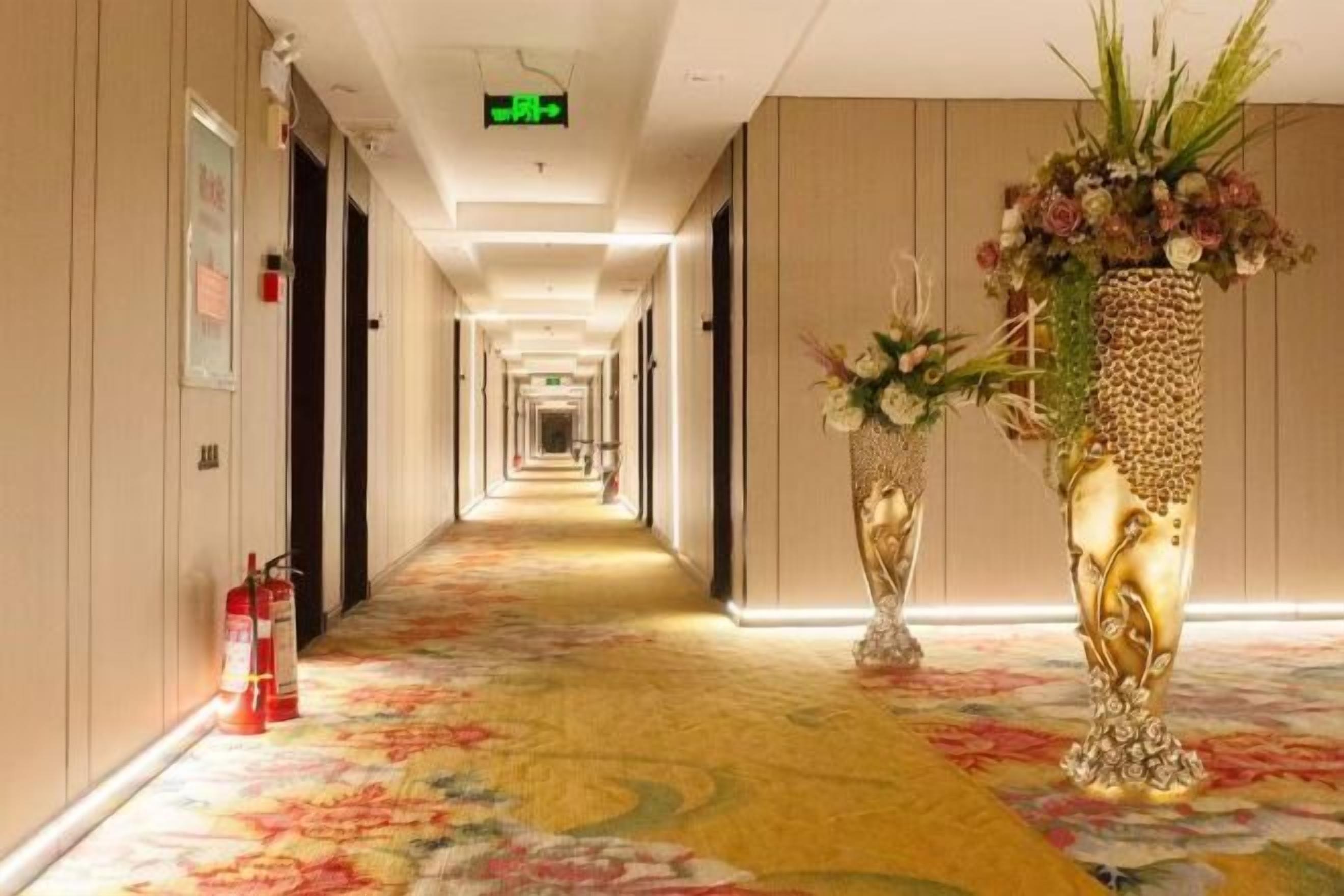A hotel corridor with a floral carpet, a fire extinguisher, and a decorative vase.