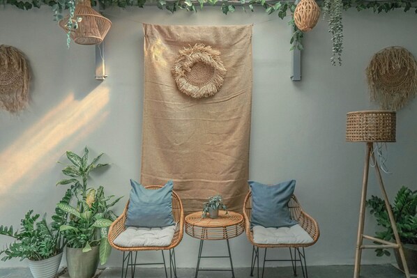 Une pièce décorée d’une grande tapisserie tissée, de fauteuils en osier avec des coussins et de plantes en pot.