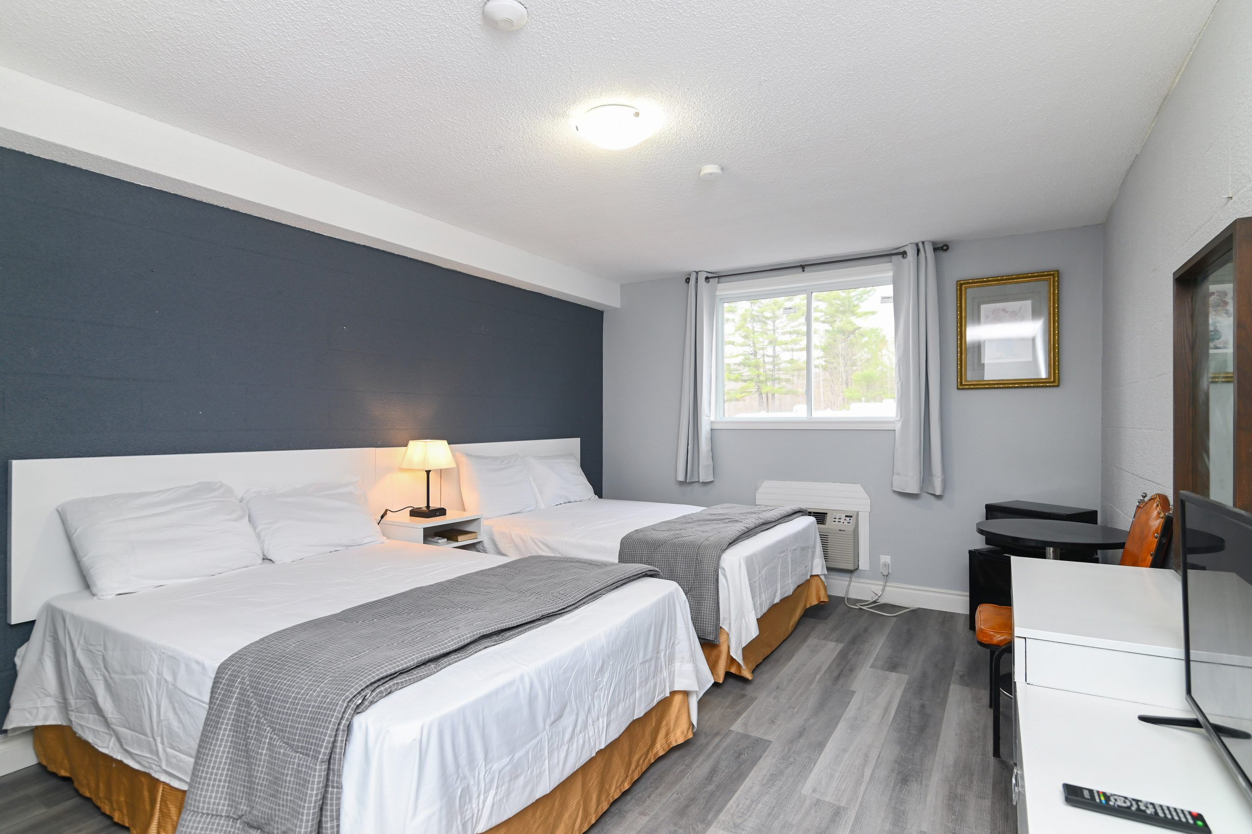 A hotel room with two beds, a desk, a chair, a TV, and a window with curtains.