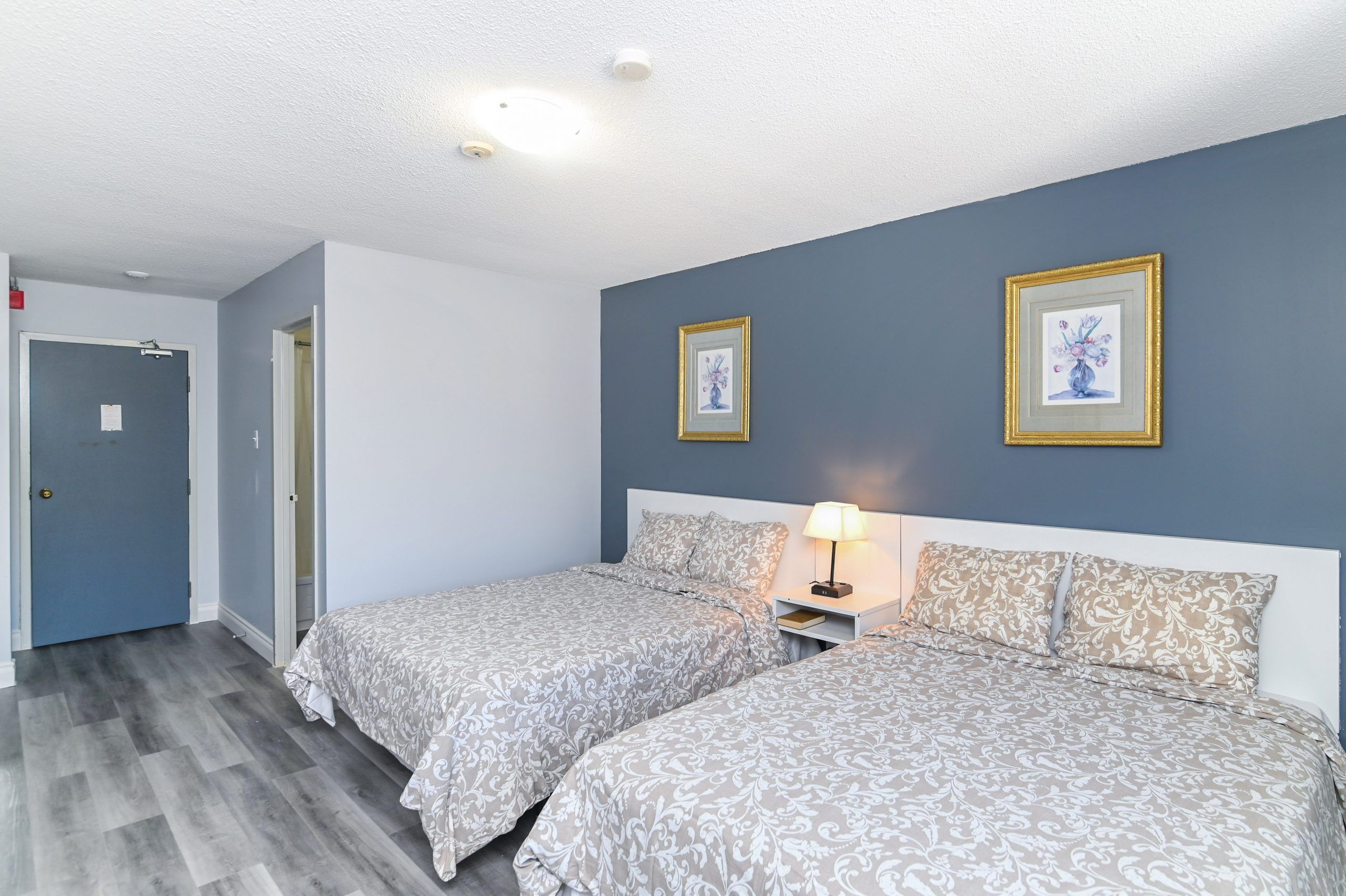 Een hotelkamer met twee bedden, een nachtkastje met een lamp en twee ingelijste foto’s aan de muur.