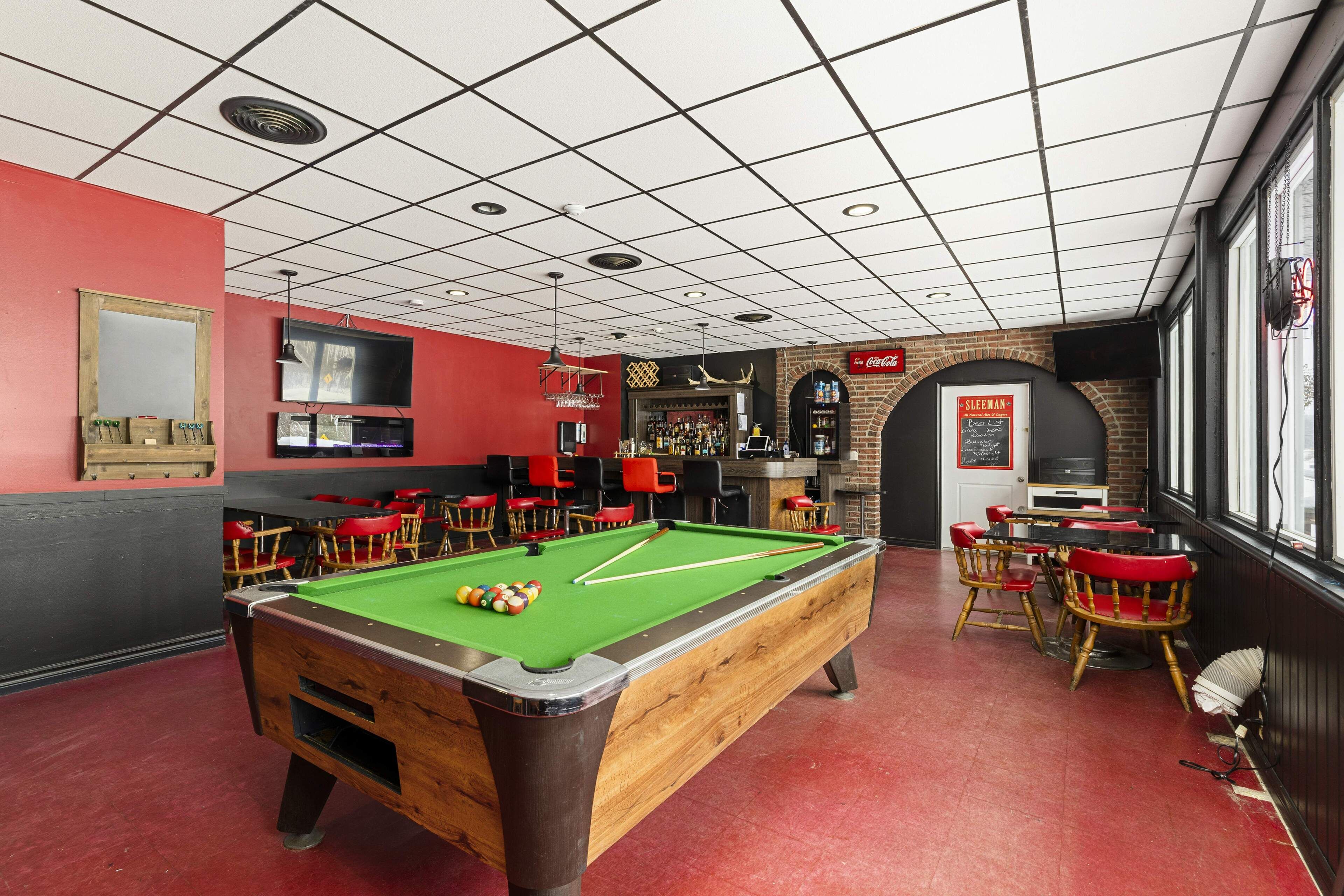 Een pooltafel in een ruimte met rode muren, een bar en een bakstenen muur met een Coca-Cola bord.