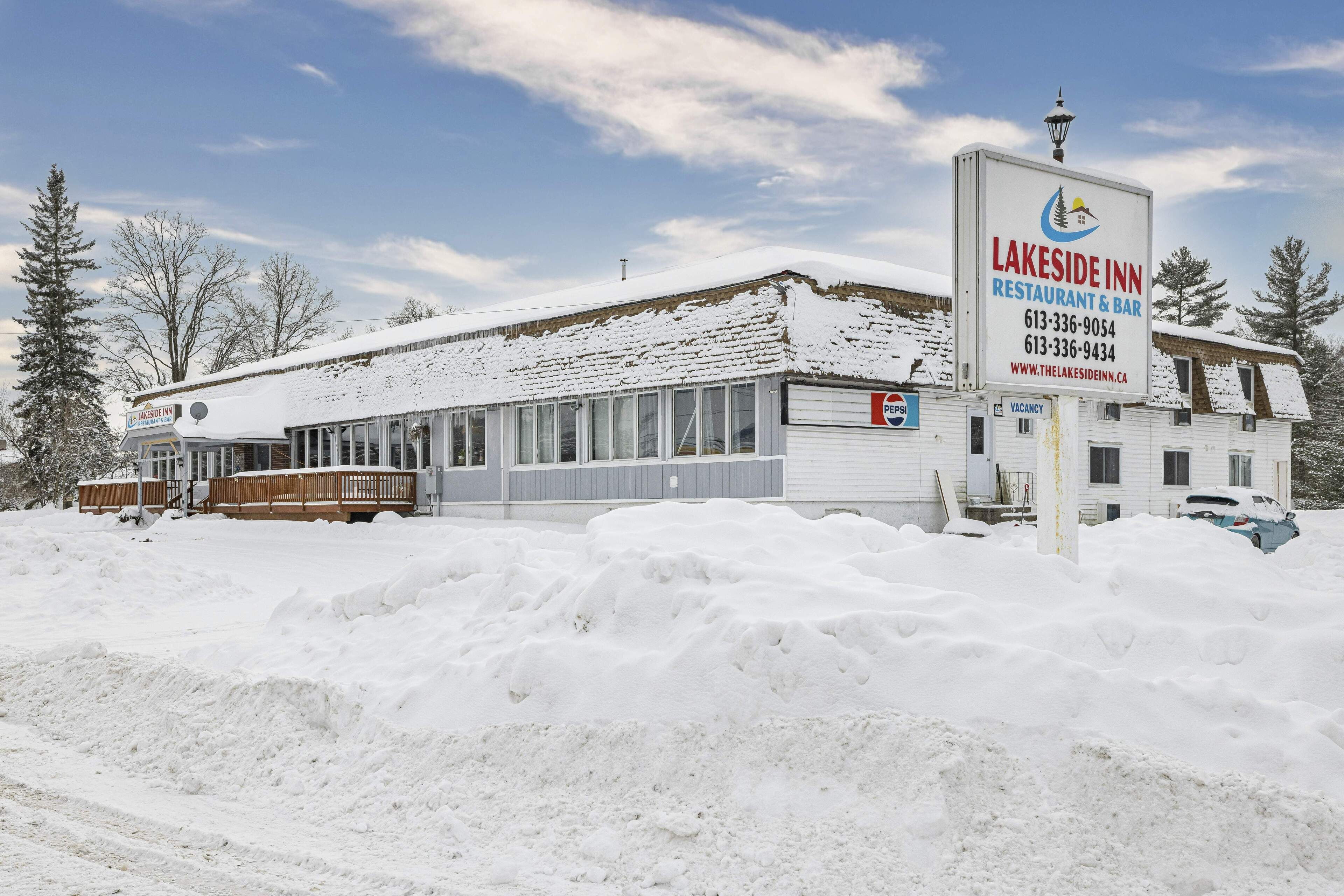 Una posada junto al lago, con un letrero grande, un porche cubierto y nieve acumulada alrededor del edificio.
