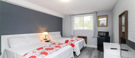 A bedroom with two beds, a desk, a mirror, and a window with curtains.