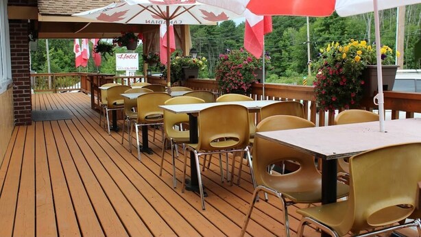 Une terrasse avec des sièges extérieurs, des drapeaux canadiens et une enseigne indiquant un hôtel.