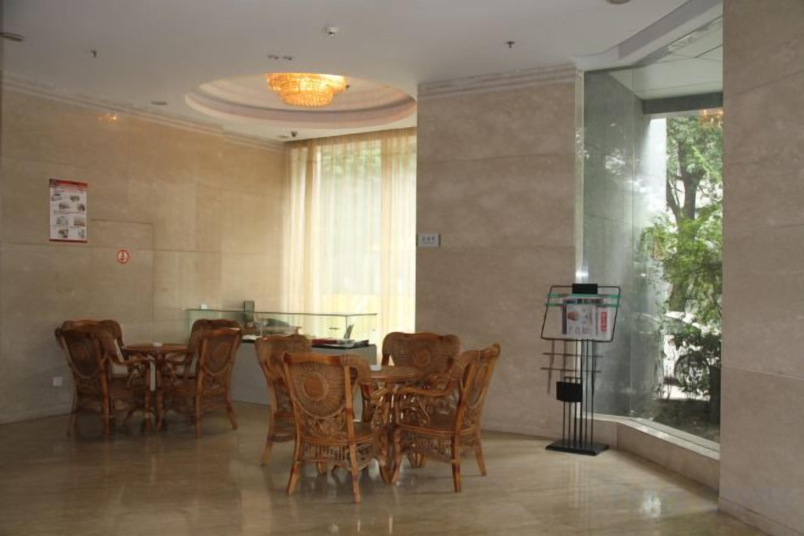 A hotel dining area with a round table and chairs, a chandelier, and a large window with a view of trees.