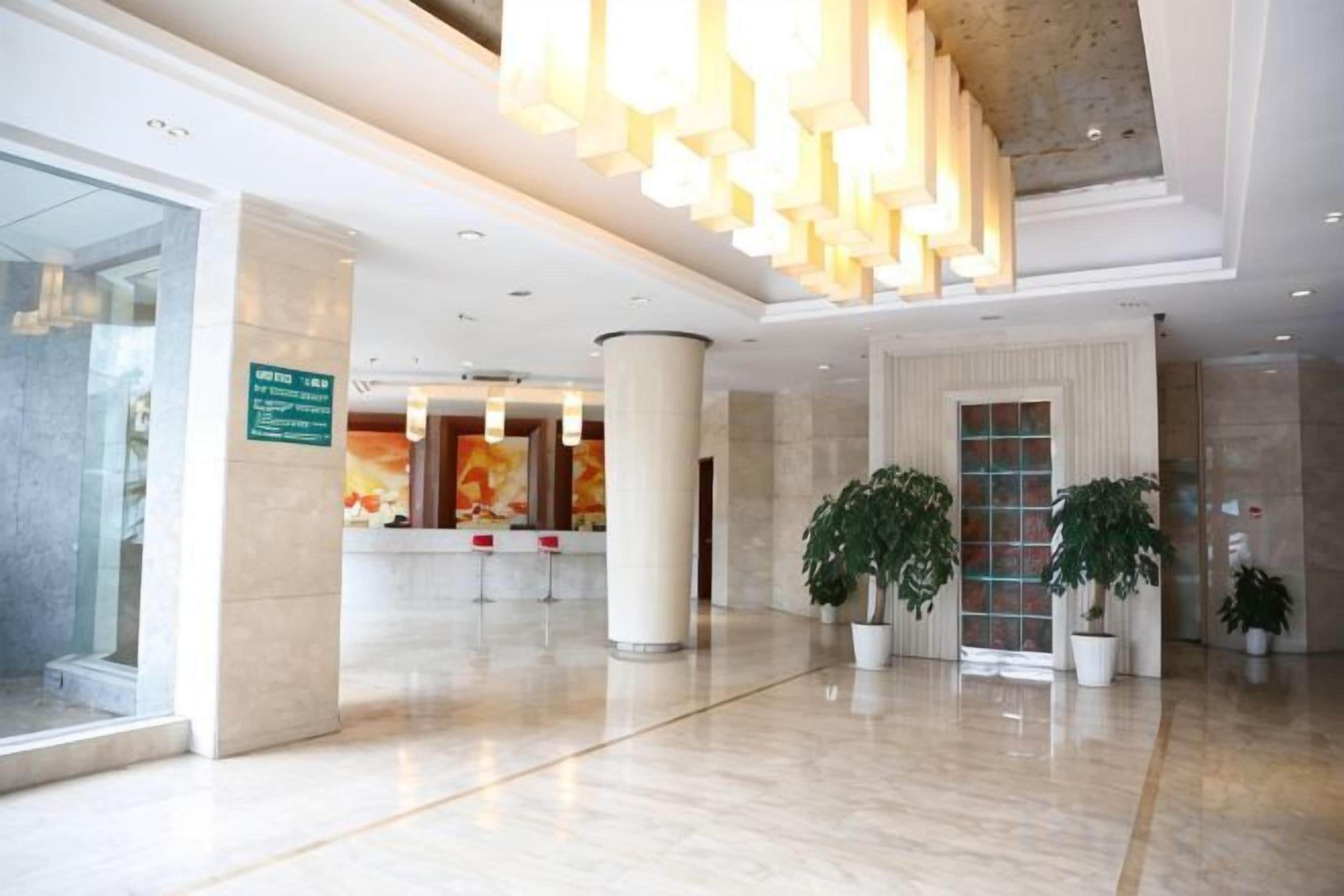 A hotel lobby with a reception desk, large columns, and potted plants.